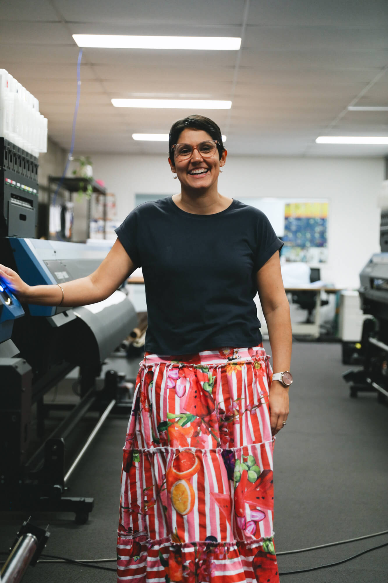 Rameez laughing in the APPLiK Brisbane digital printing studio. She is wearing a black t-shirt an da printed red, pink and yellow skirt.