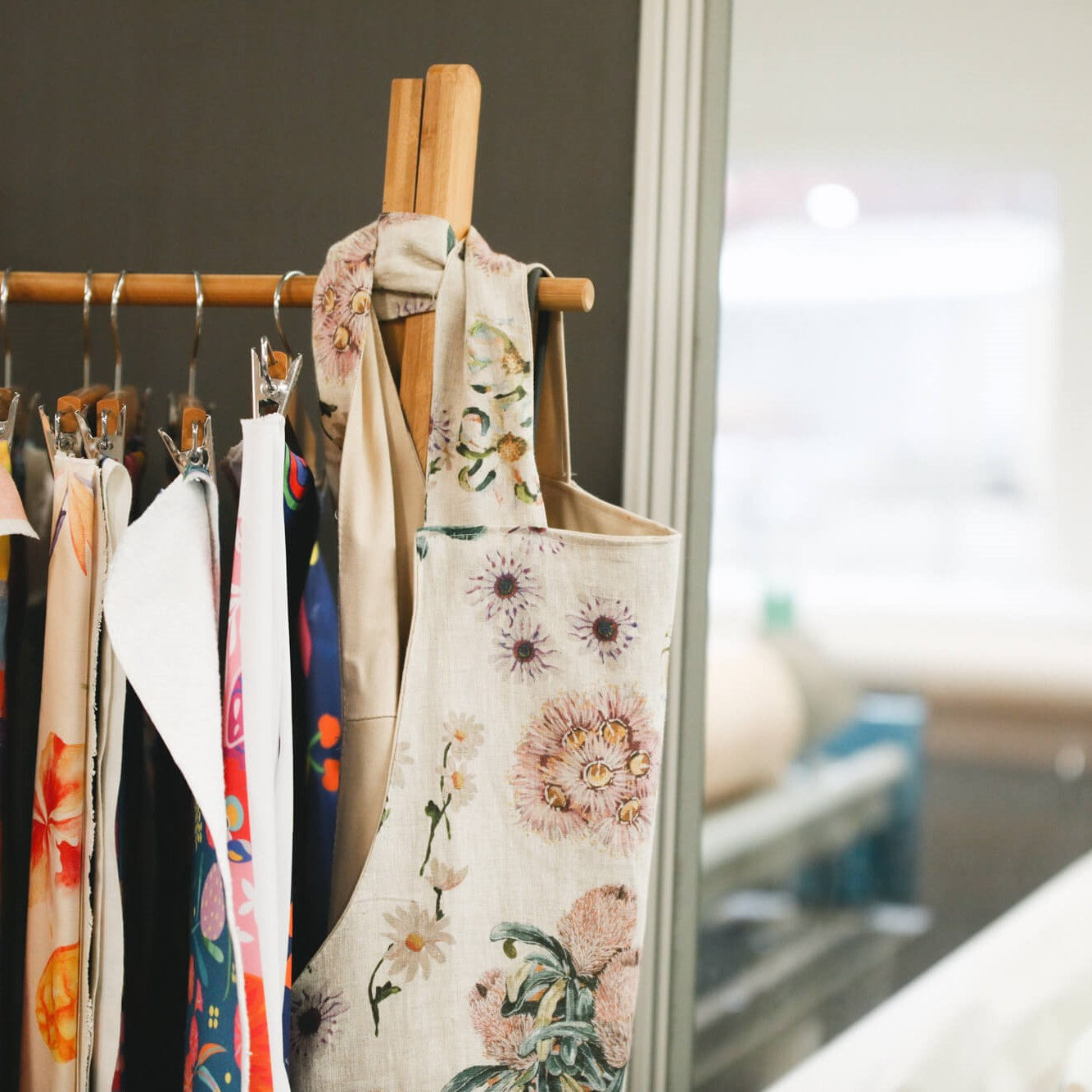A rack with hanging printed fabric and the side view of a custom-made APPLiK cross back apron.