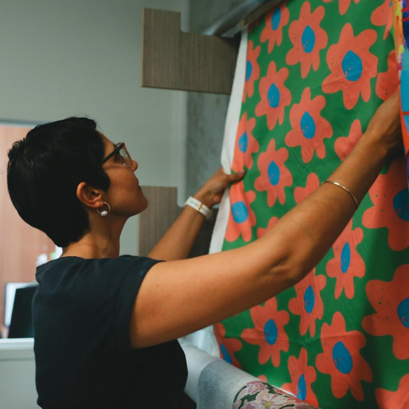 Rameez checking APPLiK digital print fabric. This artwork is bright green with orange and blue flowers.